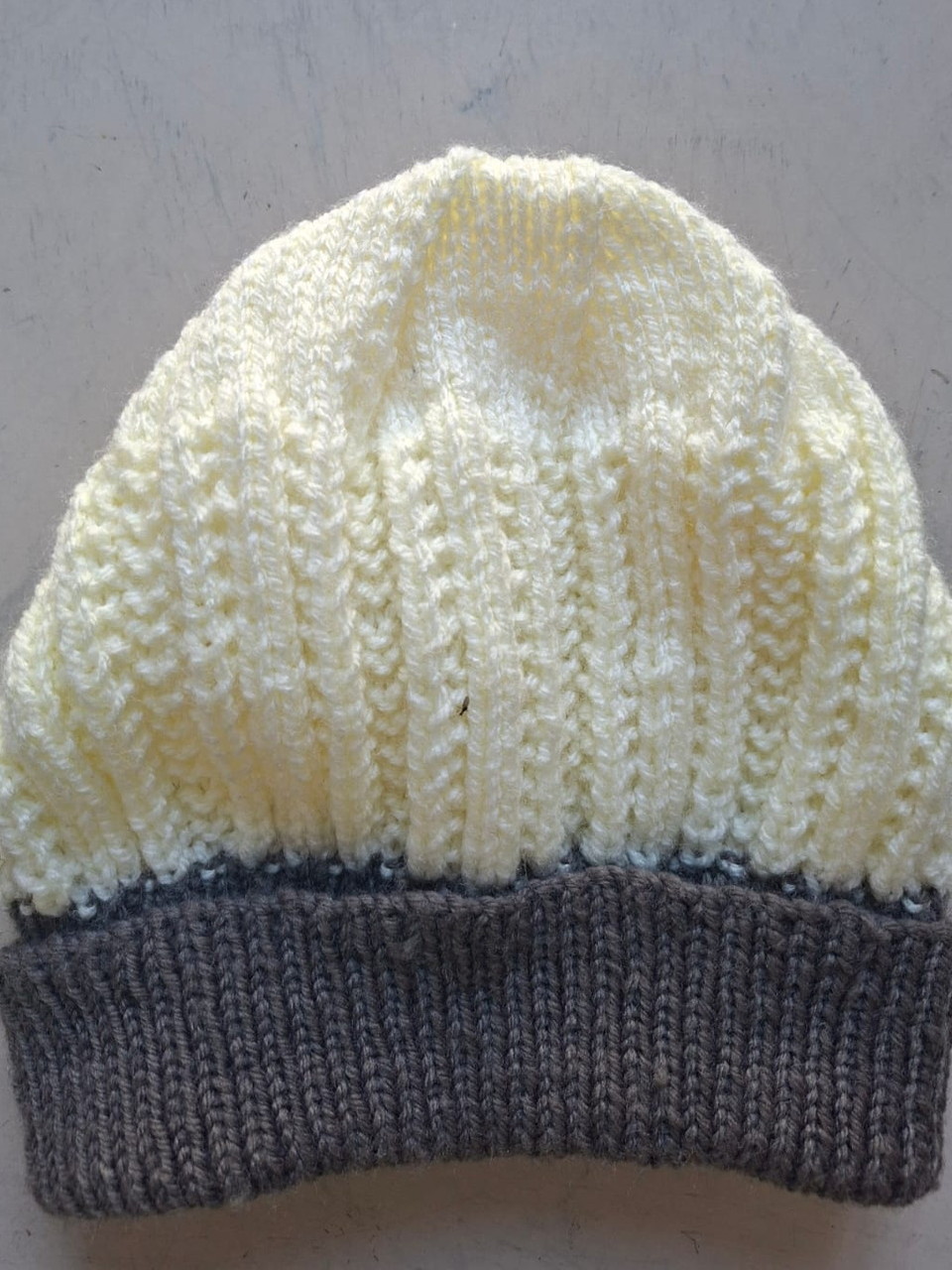 Cream beanie with a charcoal grey cuff, hand-knitted at Kranshoek