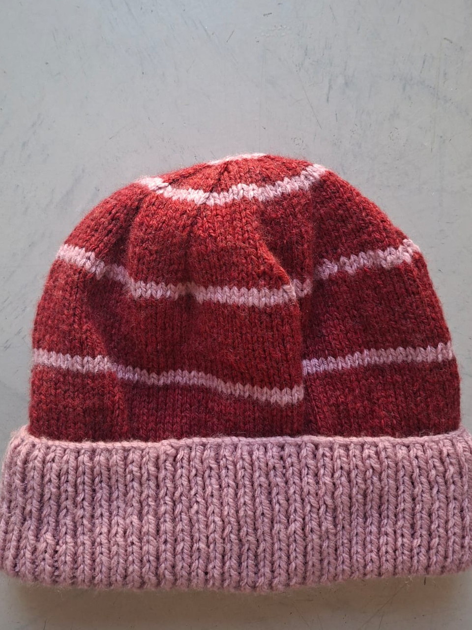 Red beanie with fine pale pink stripes and a dusty pink cuff, hand-knitted at Kranshoek