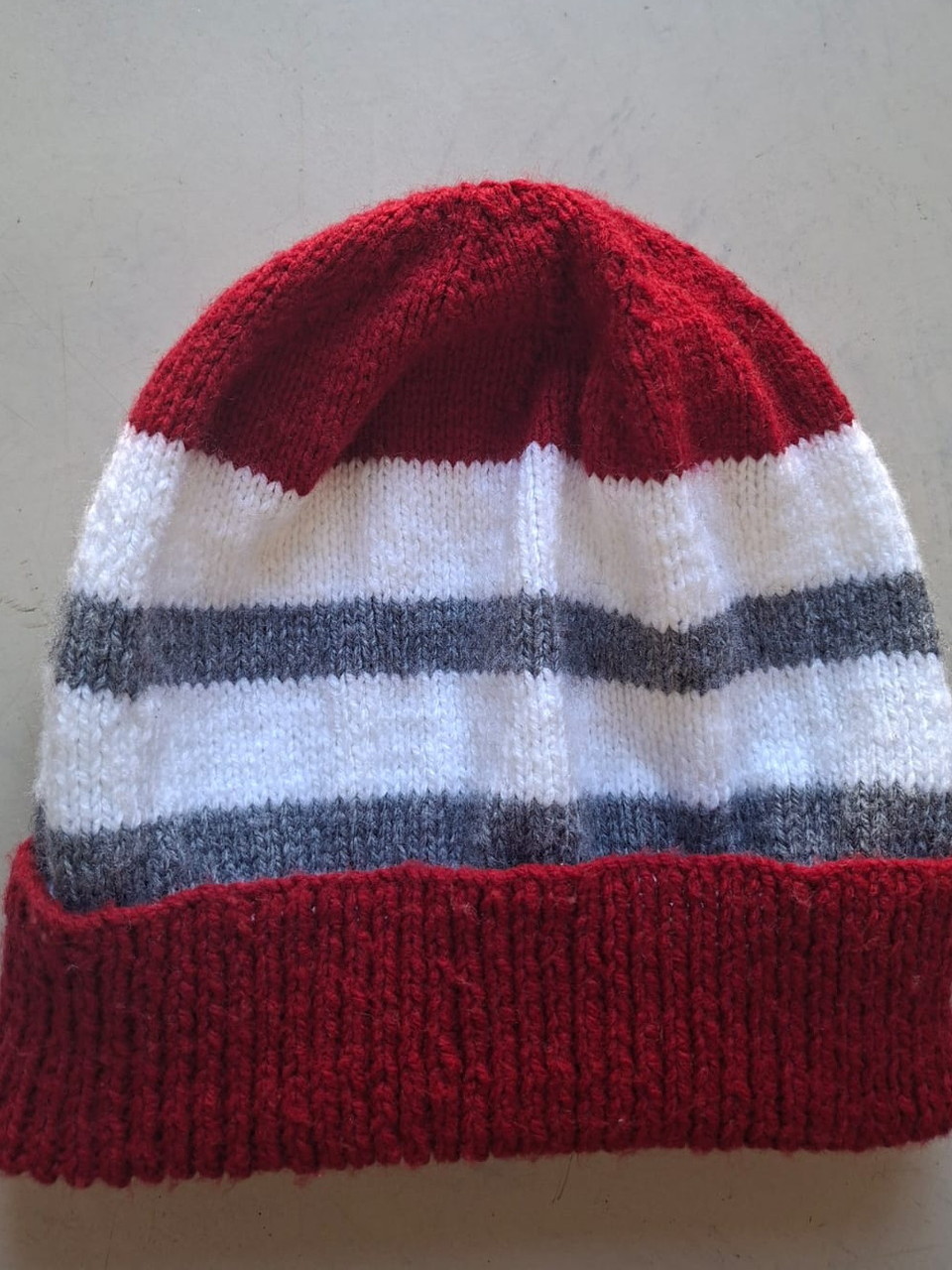 Red beanie with white and grey bands, hand-knitted at Kranshoek