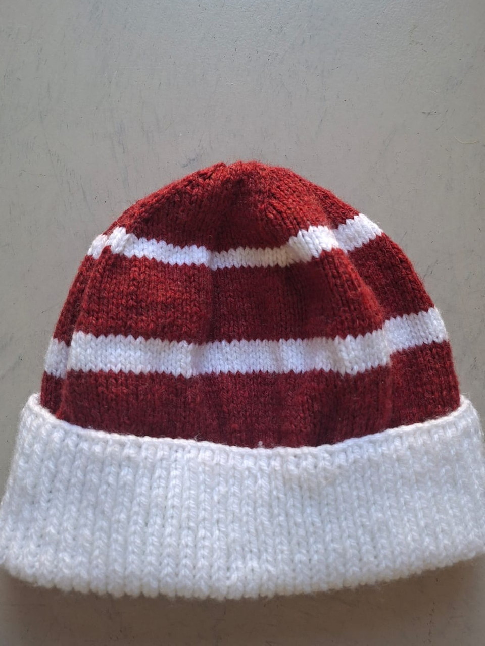 Deep red beanie with white stripes and a white cuff, hand-knitted at Kranshoek